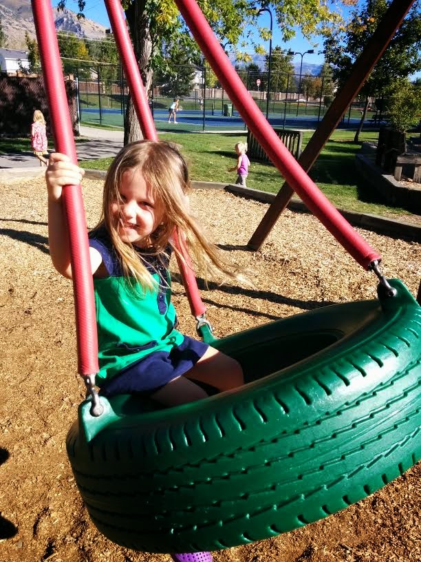 Toddler girl sitting in a tire swing at a park while laughing