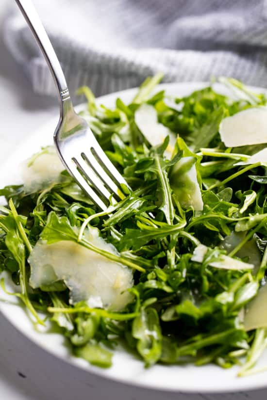 Arugula Salad served up on a white plate with a fork in it.