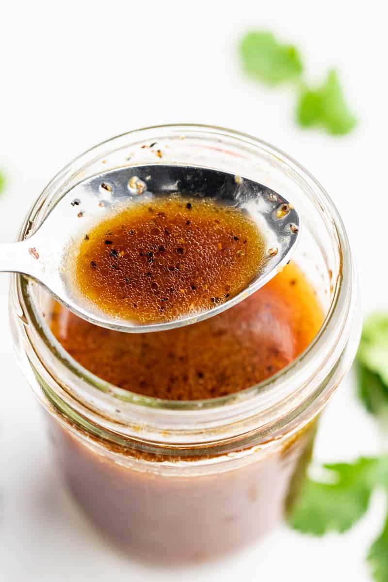 Close up overhead view of Asian dressing on a spoon hovering over a jar of the homemade dressing. 