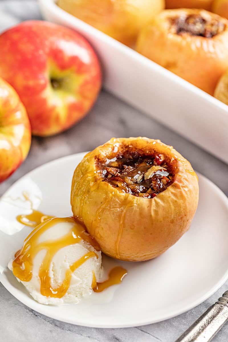 Baked apple on a white plate with a scoop of ice cream covered in caramel.