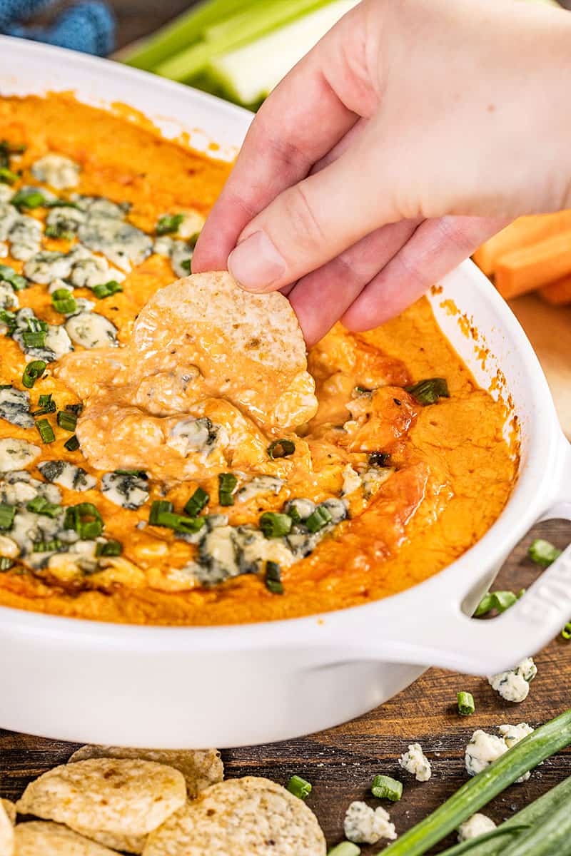 A hand dipping a chip into buffalo chicken dip.