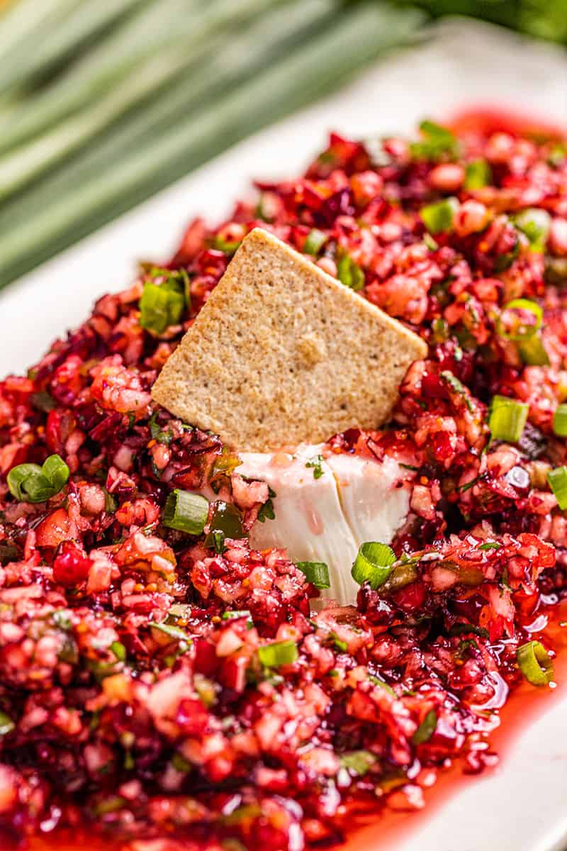 A cracker sitting on top of a block of cream cheese and cranberry salsa.