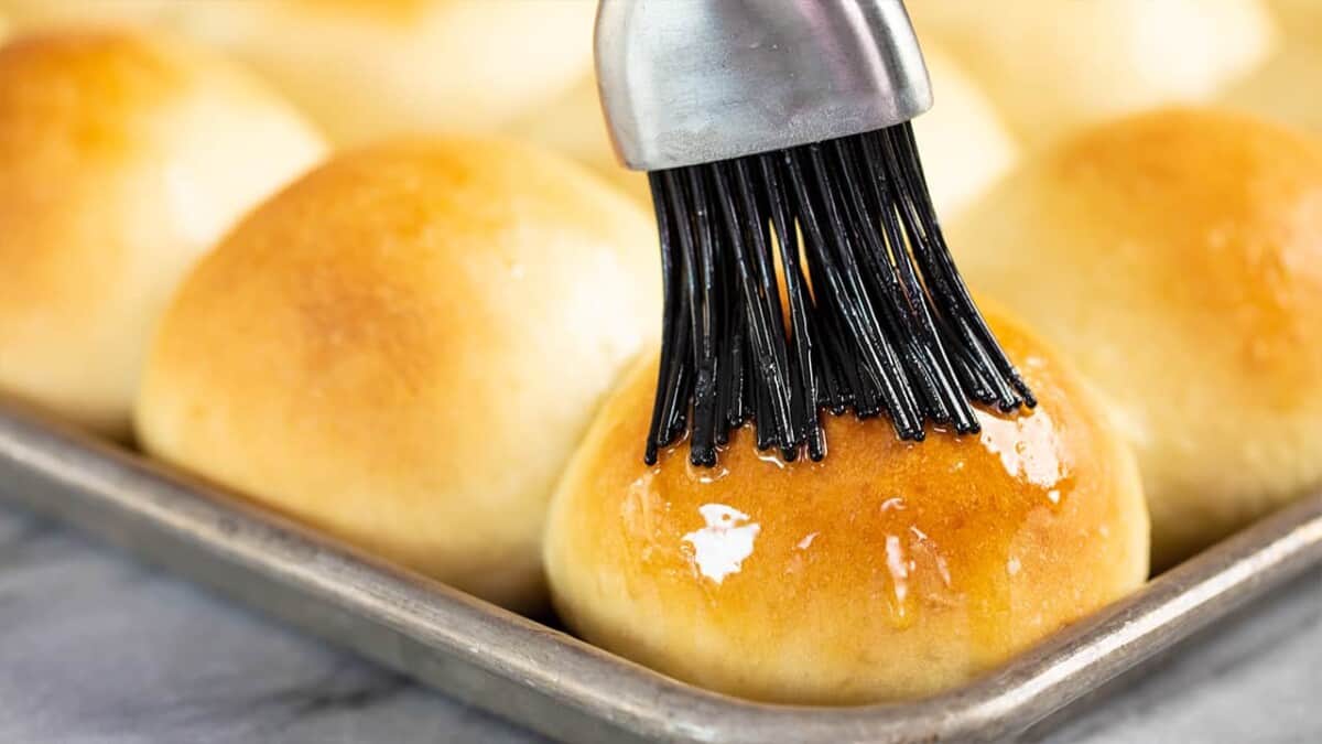 Roll being brushed with butter on a baking sheet.