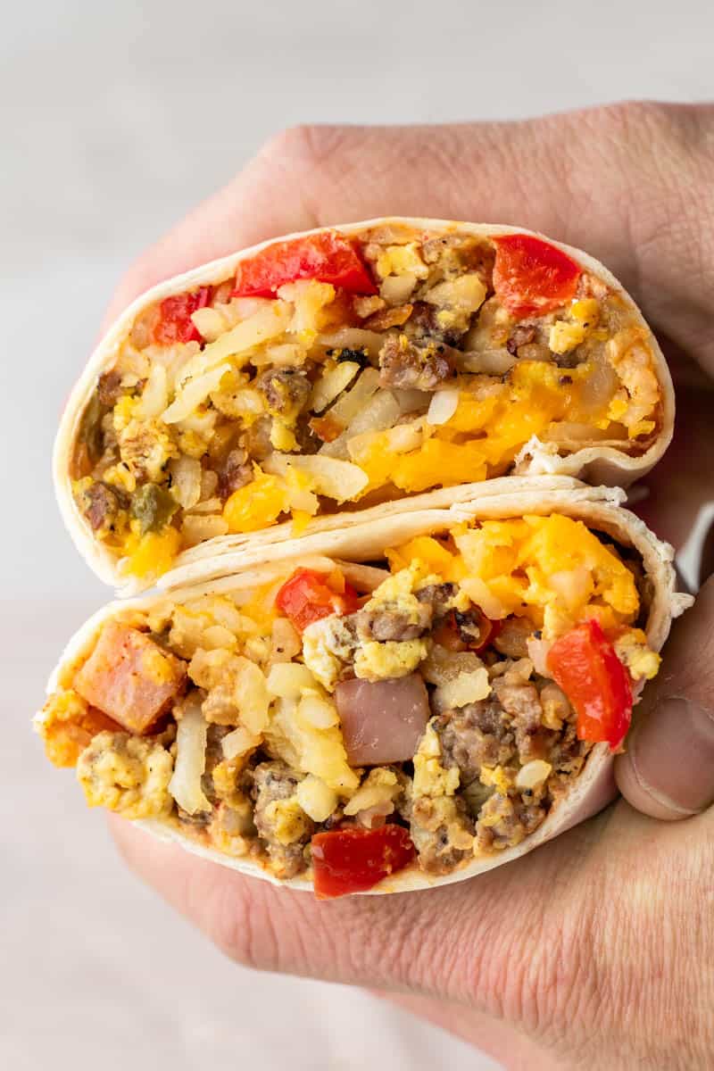 Hands holding two halves of a breakfast burrito to show the filling inside.