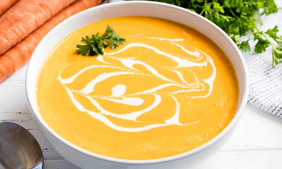 Carrot soup drizzled with cream and garnished with parsley in a white bowl