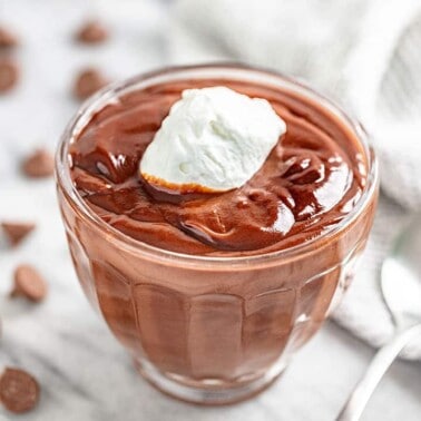 Angled view of Chocolate Pudding topped with whipped cream in a glass dish.