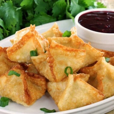 Crab Rangoons on a white plate with a dipping sauce.