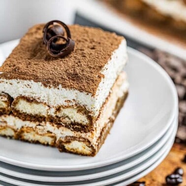 A slice of decadent tiramisu on a stack of white plates.