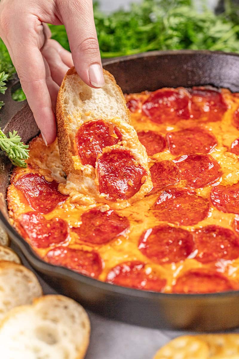 Hand dipping bread into pizza dip in a skillet