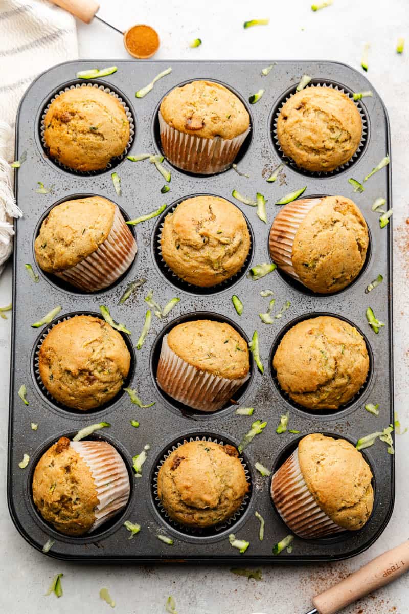 An overhead shot of a  cupcake pan with golden brown zucchini muffins with some set askew in the pan.