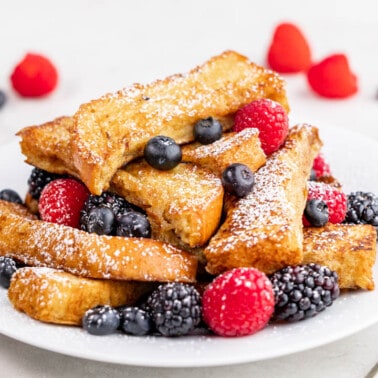 A stack of French toast sticks with fresh berries on a white plate.