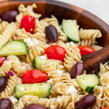 Close up view of greek pasta salad in a wood bowl.