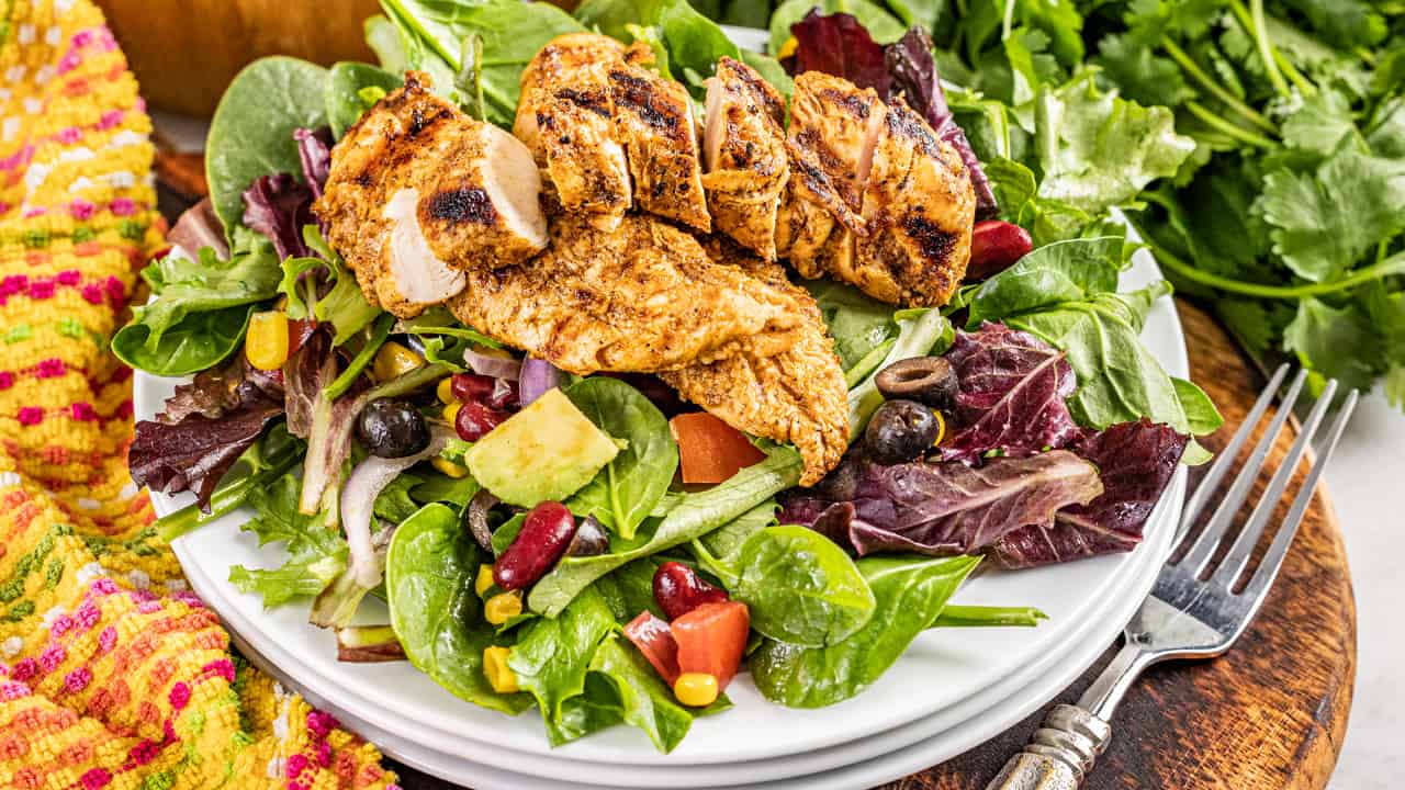 A salad on a white plate with grilled chicken on top. 