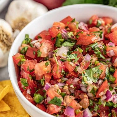 Homemade salsa in a bowl surrounded by chips and garlic