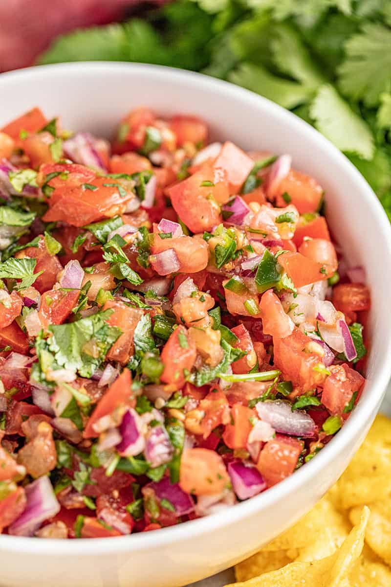 Homemade salsa in a bowl with cilantro in the background