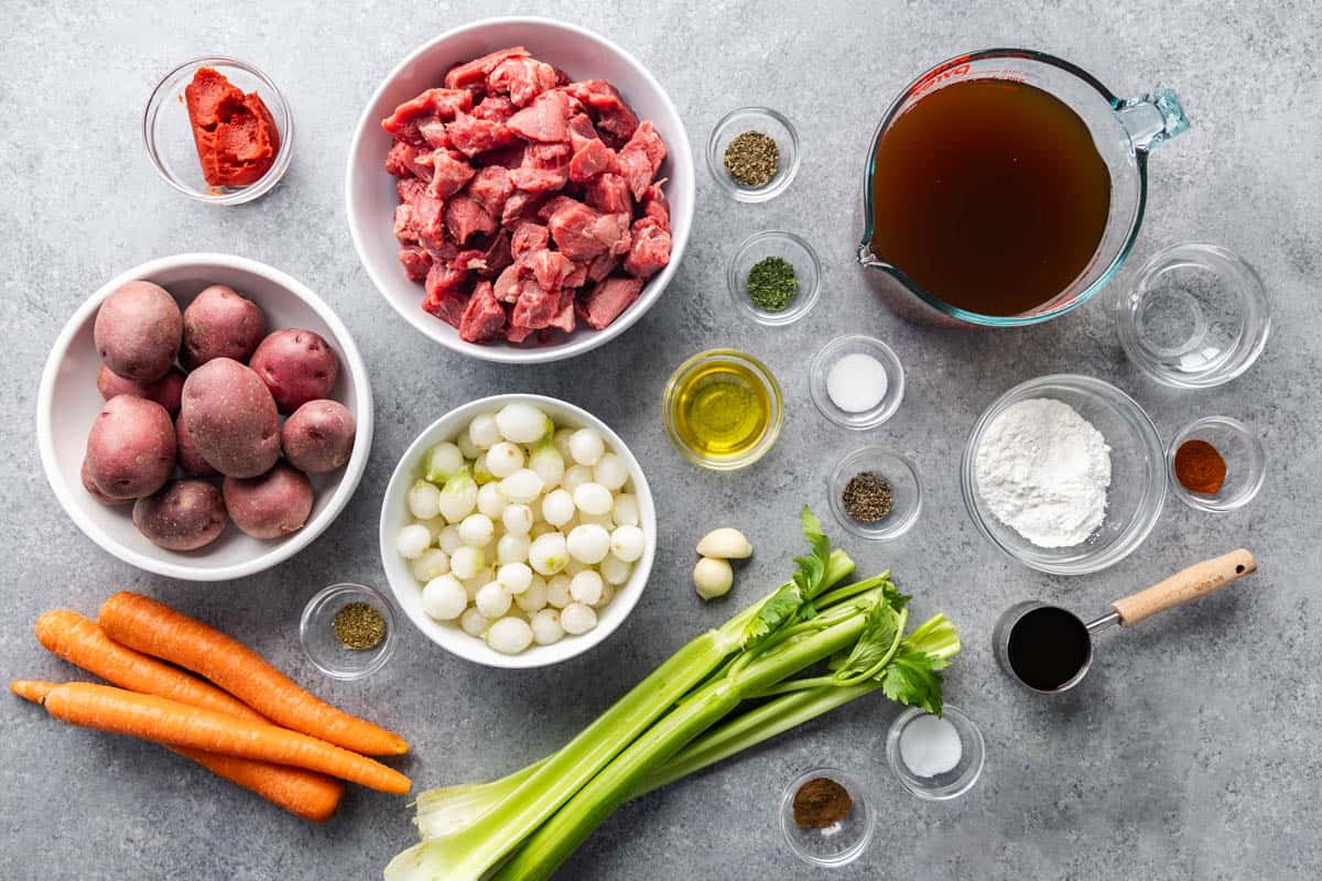 Overhead view of measured out beef, potatoes, tomato paste, carrots, onions, celery, and spices.