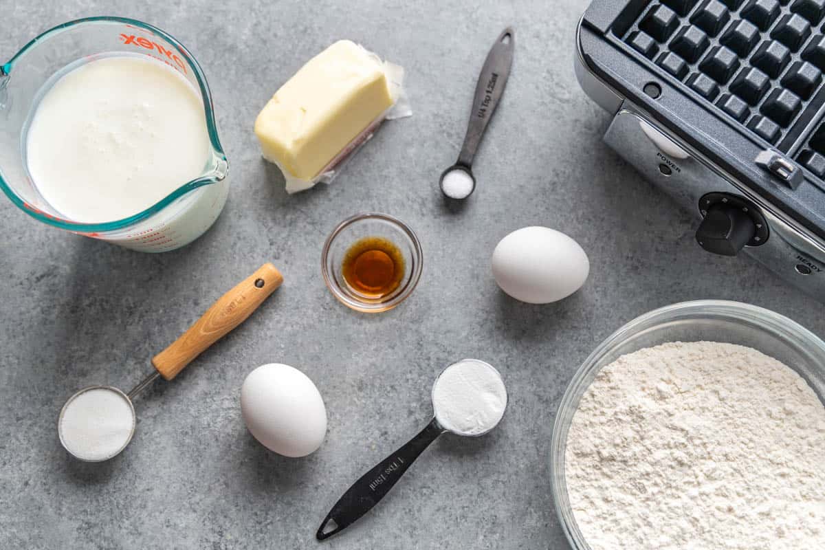 Overhead view of the raw ingredients needed to make homemade waffles on a clean kitchen counter.