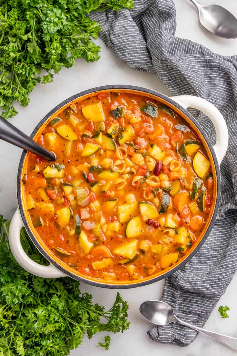 Overhead view of a white pot full of minestrone soup with a ladle sticking out.