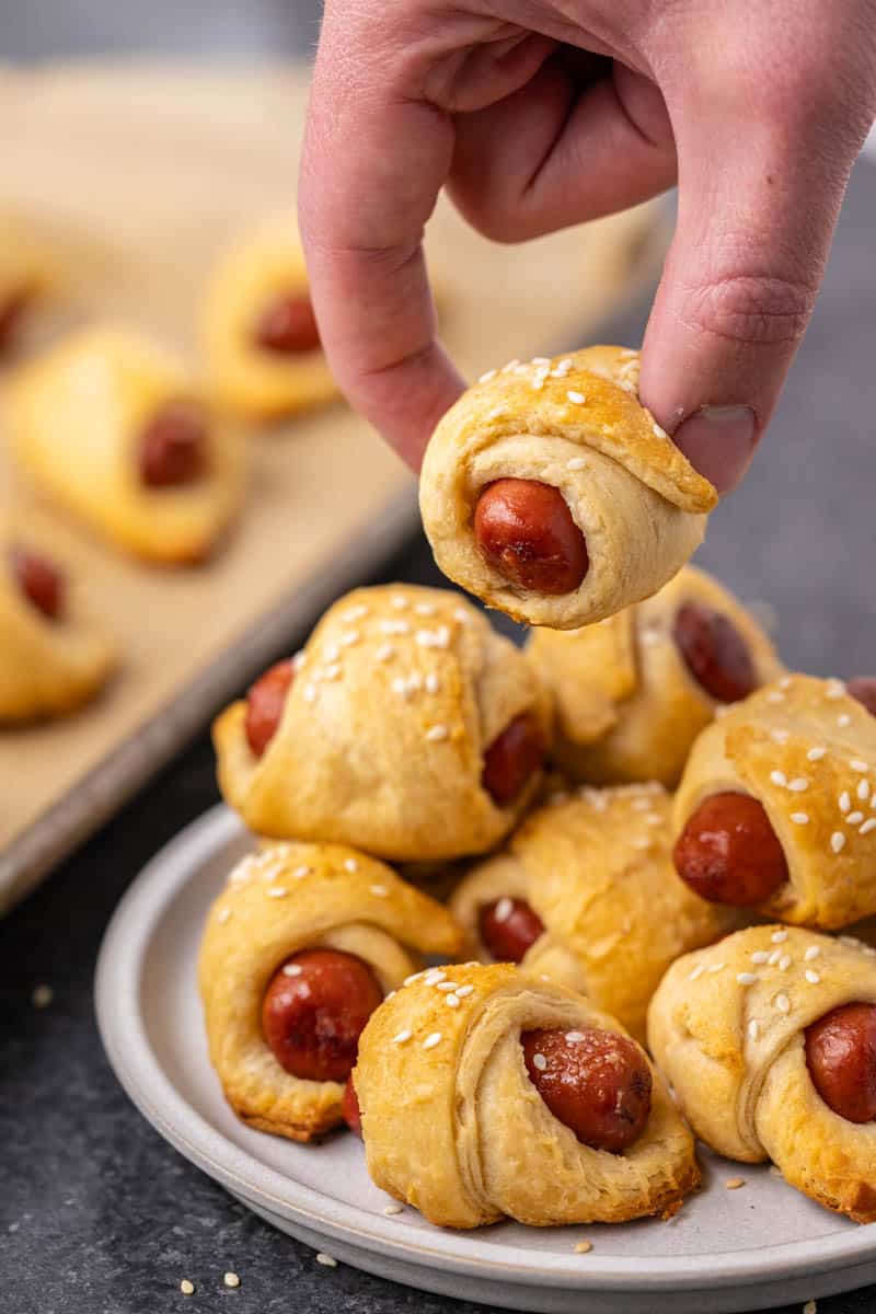 A hand picking up a pig in a blanket.