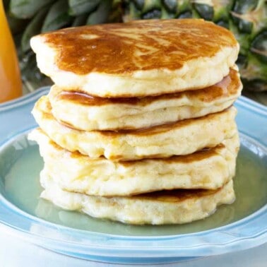 Angled view of a stack of Pineapple Pancakes on a decorative light blue plate drizzled with Coconut Syrup.