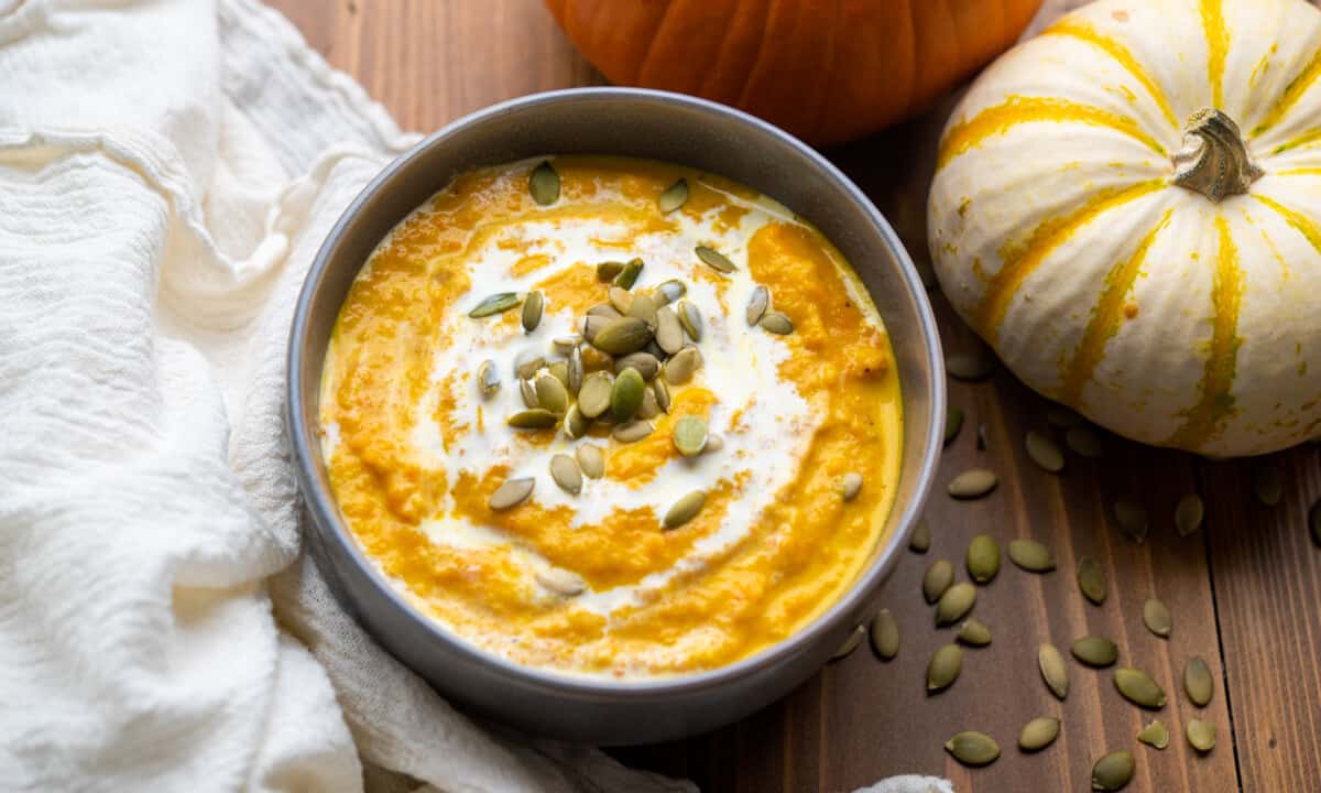 Overhead view looking into a bowl filled with creamy pumpkin soup and pumpkin seeds on top.