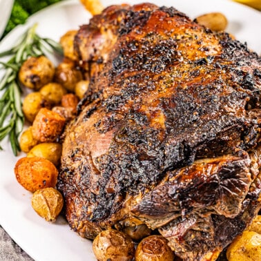 Roasted leg of lamb on a white serving platter.