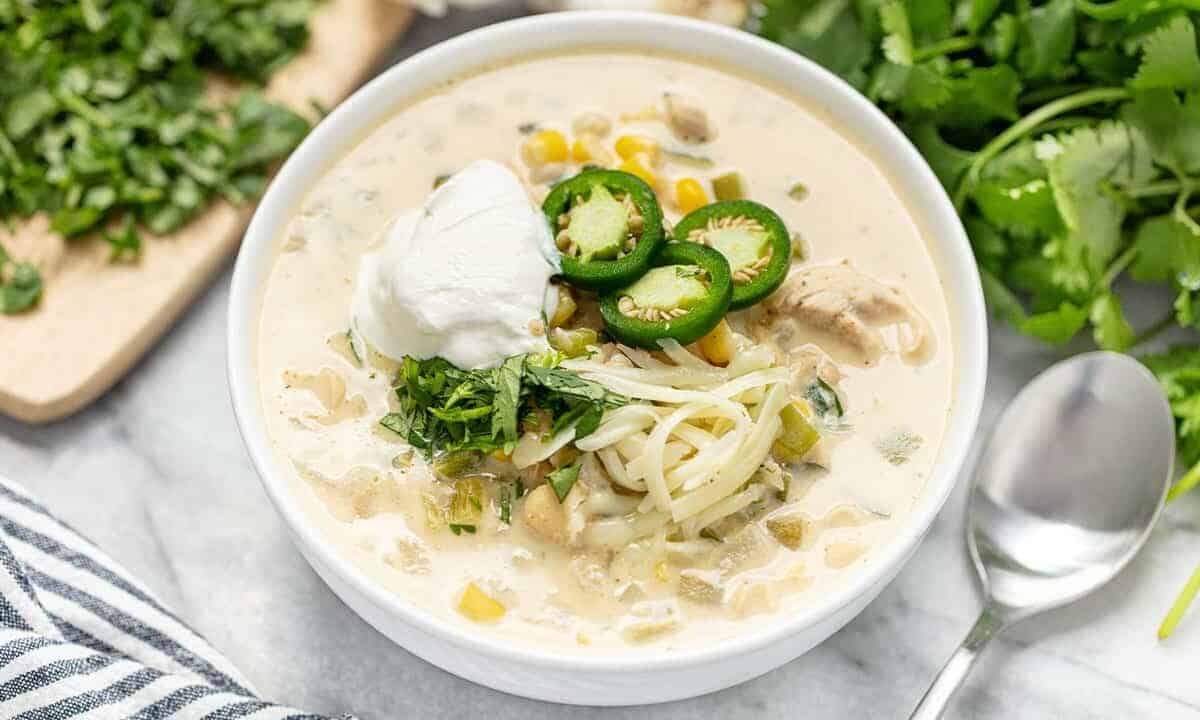 White Chicken Chili topped with cheese jalapeno slices and sourcream all in a white bowl.